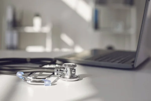 Arzt online. Ein Stethoskop liegt auf einem weißen Tisch mit einem Laptop in Unschärfe im Krankenhauszimmer. — Stockfoto