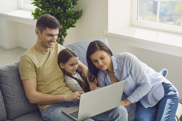 Föräldrar och dotter har kul att koppla av titta på video gör ett online-samtal till den bärbara datorn ler hemma. — Stockfoto