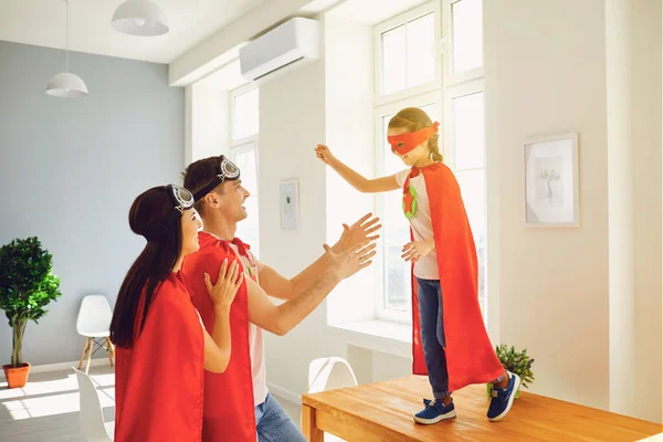Família feliz de super-heróis jogando em um quarto dentro de casa . — Fotografia de Stock