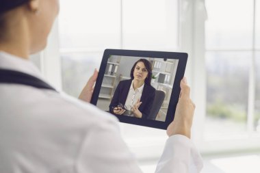 Doktor hatta. Tablet video kullanan kadın doktor, iş kadınının uzaktan hastasıyla konuşuyor..