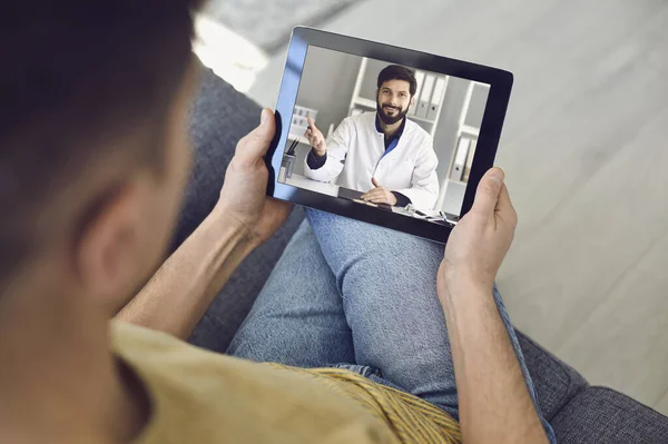 Consulenza medica online per i pazienti. Medico uomo videochiamata utilizzando computer portatile parla con il paziente maschio seduto sul divano a casa . — Foto Stock