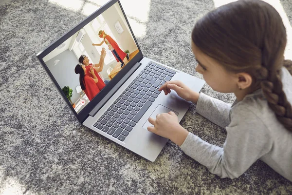 A child uses a laptop to watch home videos in a room on the floor.