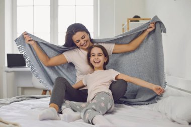 Anneler Günün kutlu olsun. Neşeli bir anne ve kız, yatak odasındaki yatakta otururken gülüyorlar..