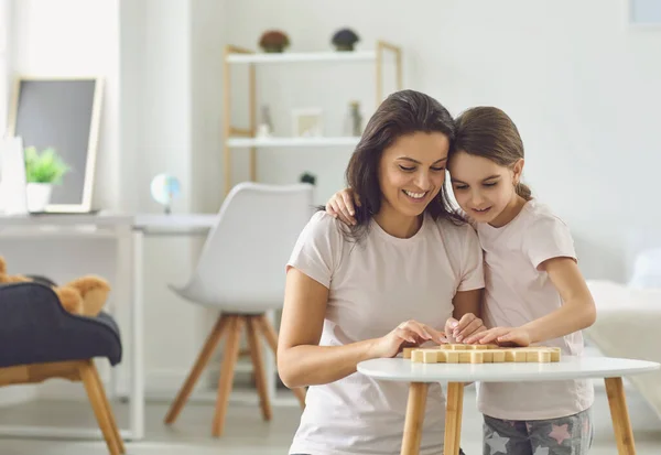 Moeder en dochter in pyjama spelen bordspellen terwijl ze aan een tafel in de woonkamer zitten. — Stockfoto