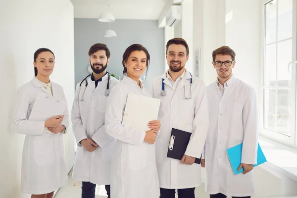 A group of confident practicing doctors in white coats are smiling against the backdrop of the clinic.