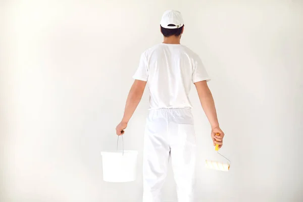 Чоловік-художник у білій формі з роликом працює в руці в білій кімнаті — стокове фото