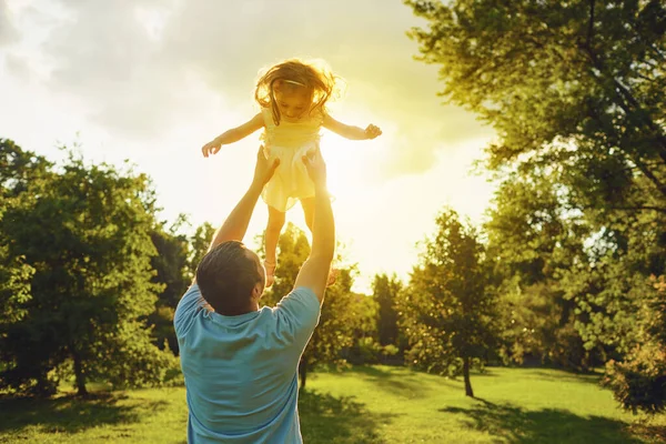 Apák napja. Apa feldobja a lányát naplementekor a nyári parkban.. — Stock Fotó