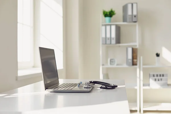 Doctor online. A stethoscope is on a white table with a laptop in blur at the hospital office. — Stock Photo, Image