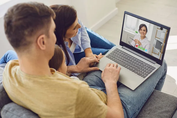 Läkarkonsultation online för anhöriga. Läkare kvinna videosamtal med bärbar dator samtal med familjen sitter på soffan hemma. — Stockfoto