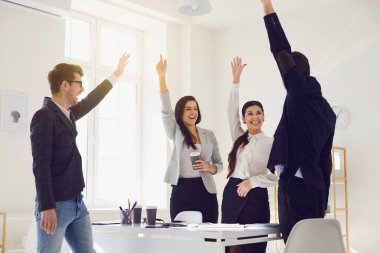 Bir grup iş adamı gülümseyerek ellerini kaldırdı. Ofisteki bir masada mutlu bir şekilde duruyorlardı..