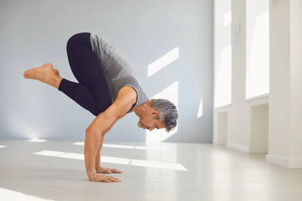 Hombre del yoga. Un hombre está practicando el equilibrio del yoga en una habitación gris. —  Fotos de Stock
