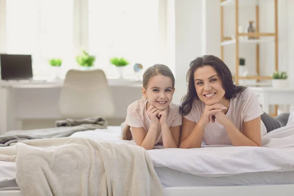 행복 한 엄마들. 어머니와 딸은 침대에 누워 카메라를 보면서 웃고 있다. — 스톡 사진