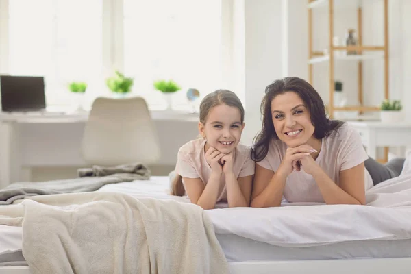 Hari ibu bahagia. Ibu dan anak tersenyum sambil melihat kamera di tempat tidur di kamar. — Stok Foto