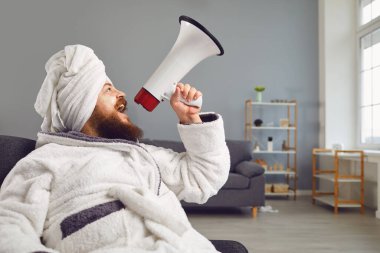 Komik güzellik maskesi kozmetik pedikür konsepti. Bornozlu ve havlulu komik şişman adam megafonla bağırıyor. Evdeki güzellik salonunda oturuyor..