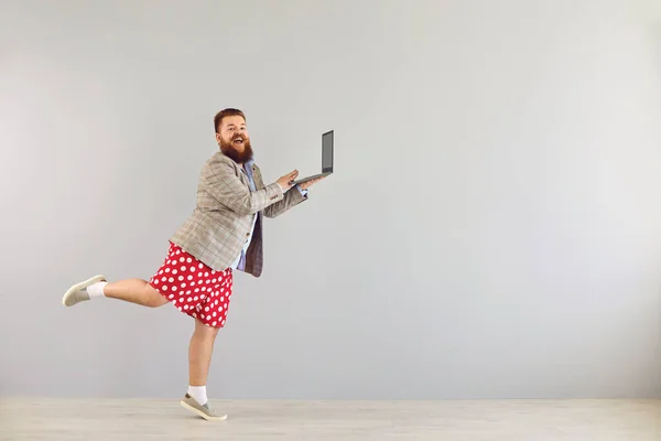 Lustiger dicker Mann in Jacke arbeitet mit einem Laptop, während er auf grauem Hintergrund tanzt. — Stockfoto