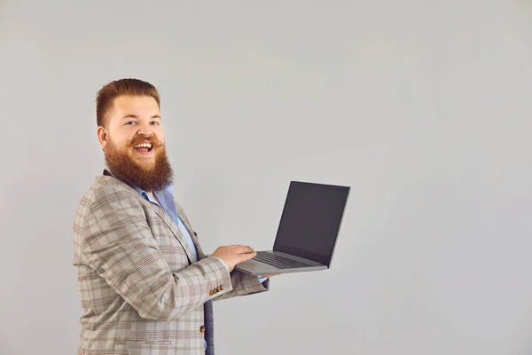 Lustiger dicker Mann in Jacke arbeitet mit einem Laptop, während er auf einem grauen Hintergrund steht. — Stockfoto