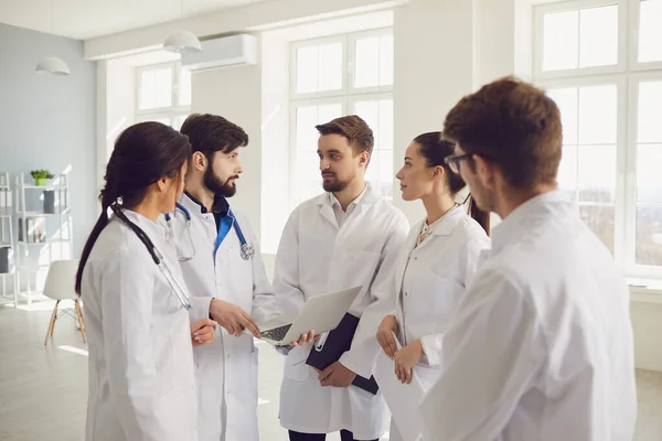 Grupo de médicos praticantes em uma reunião discutir o diagnóstico de um paciente de pé em um consultório de clínica . — Fotografia de Stock