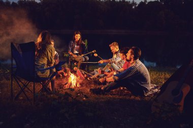 Sonbaharda yazın geceleri çadırın yanındaki şenlik ateşinin yanında oturan bir grup insan..