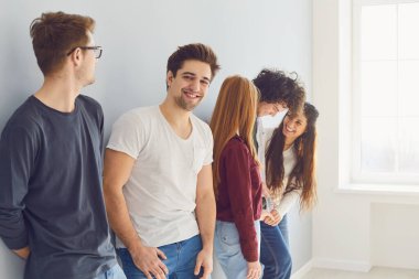Bir grup gülen arkadaş penceresi olan parlak bir odada dikiliyorlar..