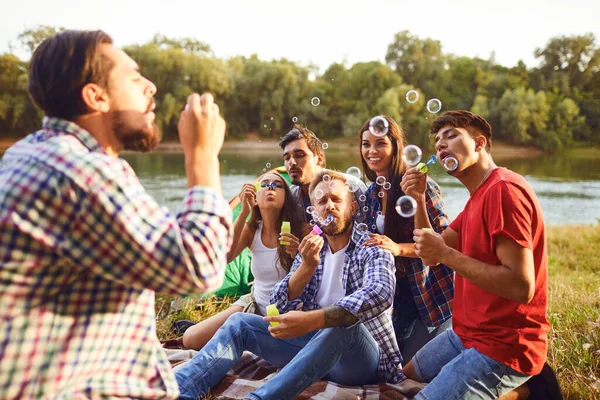 Young people make soap bubbles while sitting on the grass on in nature. — Stock Photo, Image