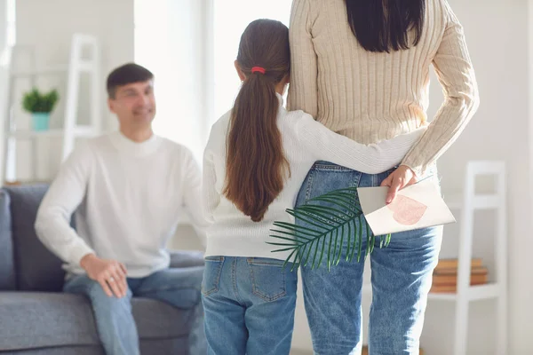 Gelukkige vaders.Achteraanzicht. Moeder en kind dochter feliciteert vader met een ansichtkaart in een kamer met een raam. — Stockfoto