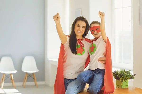 Dia das Mães. Menina e mãe em super-herói traje abraço sorrindo no quarto . — Fotografia de Stock