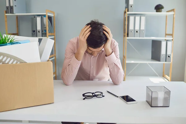 Desempleo. Despido. Empresario despedido está molesto con una caja de cartón sosteniendo su cabeza en sus manos mientras está sentado en una oficina de la empresa. —  Fotos de Stock