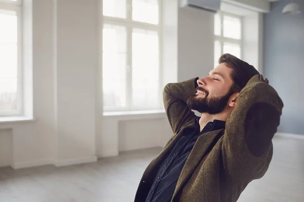 Een man in een zakenman pak ontspant in een kantoor met handen omhoog achter zijn hoofd. — Stockfoto