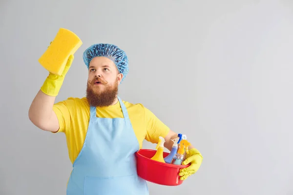 Lustiger dicker Mann mit Bart in Schürze räumt vor grauem Hintergrund auf. — Stockfoto