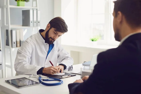 Patient beim Arztbesuch in der Klinik. Ärztliche Arbeit schreibt ein Rezept auf einen Tisch im Krankenhaus. — Stockfoto