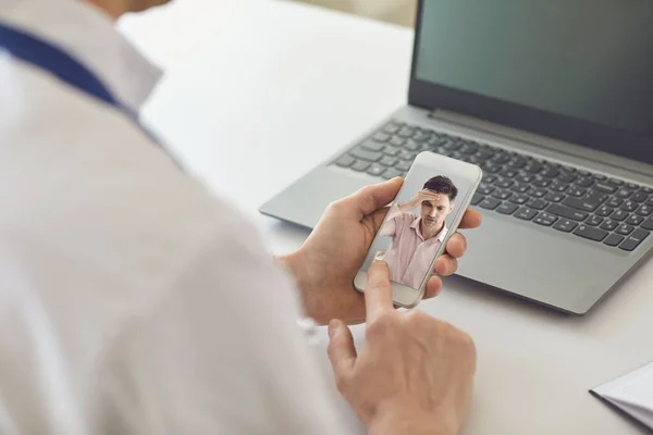 Médico en línea. El doctor habla con un paciente usando un teléfono sentado detrás de una pajita en una clínica. Consulta médica en línea . — Foto de Stock