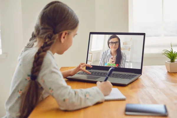 A gyermekek online oktatása. Lány iskoláslány tanít egy leckét online segítségével egy laptop video chat call konferencia egy tanár otthon. — Stock Fotó