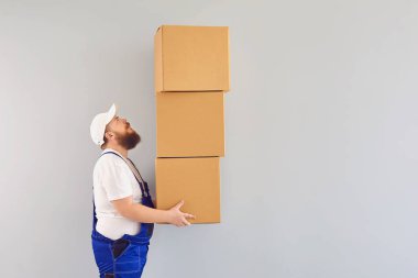 Mavi üniformalı, gri arka planda karton kutulu komik, şişman, sakallı bir kurye yükleyici..