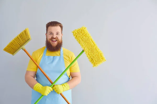 Önlüklü, sakallı, komik, şişman bir adam gri arka planı temizliyor.. — Stok fotoğraf
