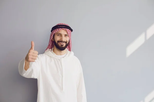 Vonzó mosolygós arab férfi mutatja hüvelykujját fel szürke háttér — Stock Fotó