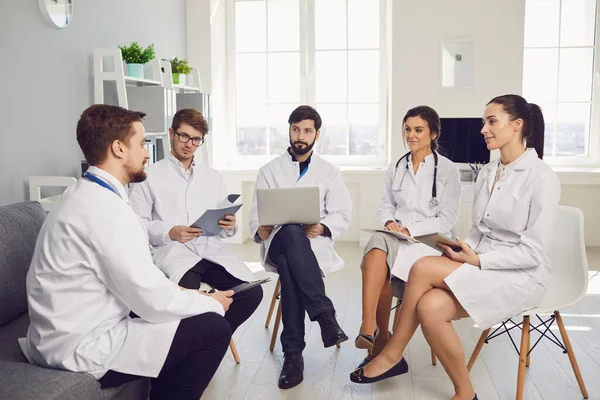 Group of practicing doctors in a meeting discuss the diagnosis of a patient standing in a clinic office.