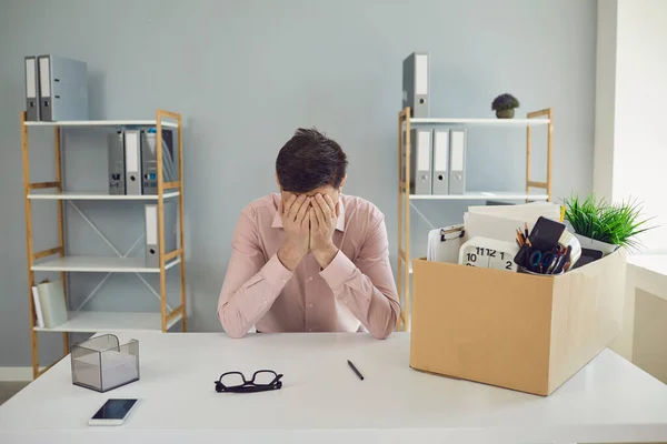 失業だ。解雇だ。解雇されたビジネスマンは、会社のオフィスに座っている間、彼の手に頭を持って段ボール箱に動揺しています. — ストック写真