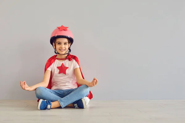 Rolig baby superhjälte skrattar medan du sitter på golvet i Lotus position. Lustiga barn yoga. — Stockfoto