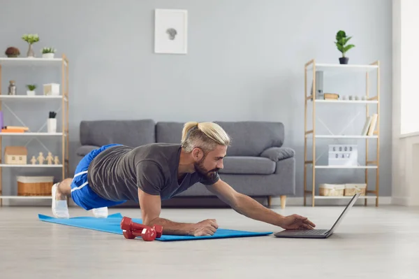 Workout exercise fitness online video call. Man doing exercises of an online fitness course training in a laptop video chat at home.