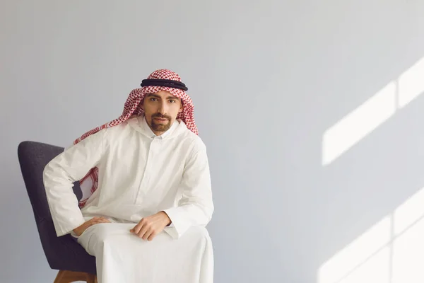 Страшный арабский бизнесмен, сидящий в кресле, думает, что смотрит на серый фон. Портрет привлекательного араба. — стоковое фото