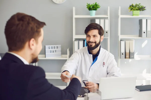 Médico confiante dá ao paciente uma receita enquanto está sentado em uma mesa em um escritório da clínica . — Fotografia de Stock