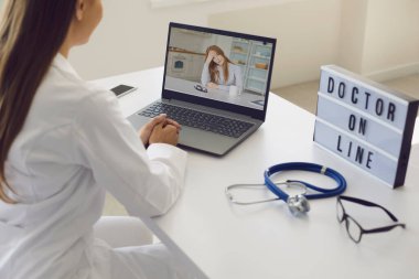Doktor hatta. Kadın doktor, hasta bir hastayı, klinikteki masada otururken bilgisayarlı görüntülü konuşma kullanarak dinliyor..