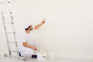 Beyaz üniformalı bir ressam odadaki resim için beyaz bir arkaplan işaret ediyor..