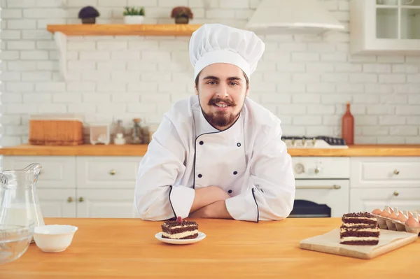 Confeiteiro homem sorri enquanto está de pé com bolo em suas mãos na padaria da cozinha — Fotografia de Stock