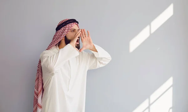 Арабский человек кричит вызовы приглашает сообщает подарки на сером фоне. A — стоковое фото