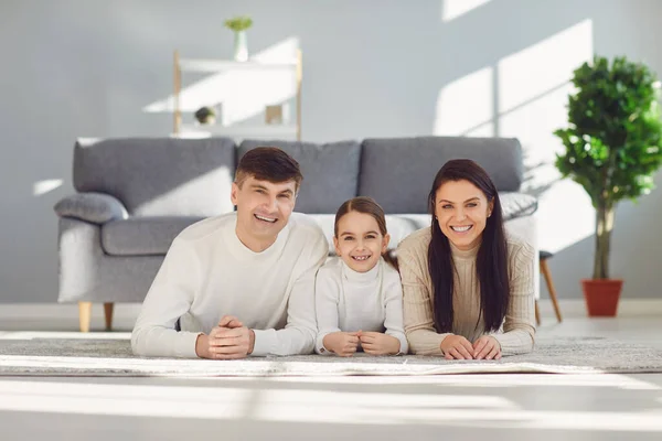 Gelukkig glimlachende familie knuffelen terwijl liggend op de vloer in de kamer thuis. C — Stockfoto