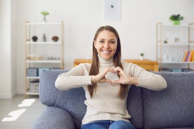 Online flört görüntülü sohbet görüşmesi. Gülümseyen kadın internetteki kameraya bakıyor. Bir randevu sitesindeki görüntülü sohbette adamın ellerini kalp şeklinde tutuyor..
