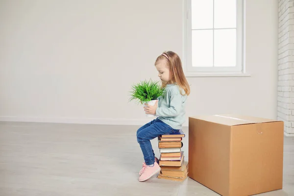 Seorang gadis anak dengan bunga duduk di kotak untuk pindah ke rumah baru. — Stok Foto