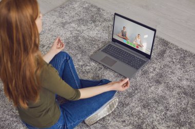 İnternetteki yoga meditasyonu. Günlük kıyafetli kız odada yoga meditasyonu yapıyor..