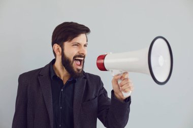 Ceketli bir adam gri arka planda megafonla bağırıyor..